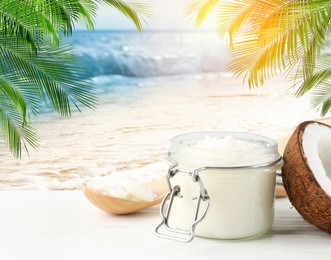 Image of Cooking oil in jar and coconut on white table against beach. Space for text
