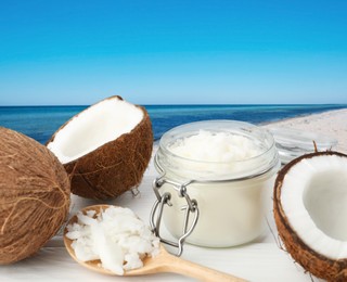 Image of Cooking oil in jar and coconuts on white table against beach