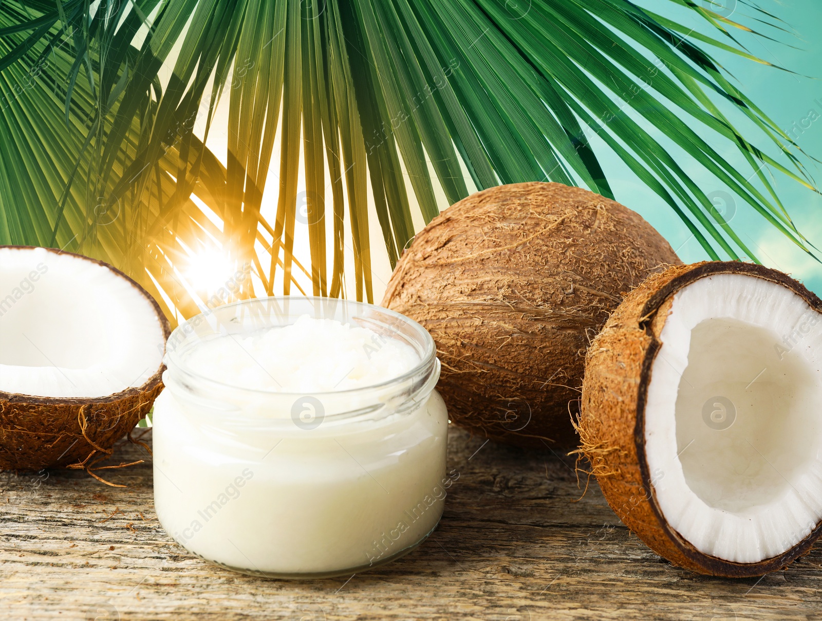 Cooking oil in jar and coconuts on wooden table against palm leaves Image of Cooking oil in jar and coconuts on wooden table against palm leaves