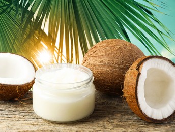 Image of Cooking oil in jar and coconuts on wooden table against palm leaves