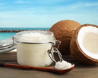 Image of Cooking oil in jar and coconuts on wooden table against beach