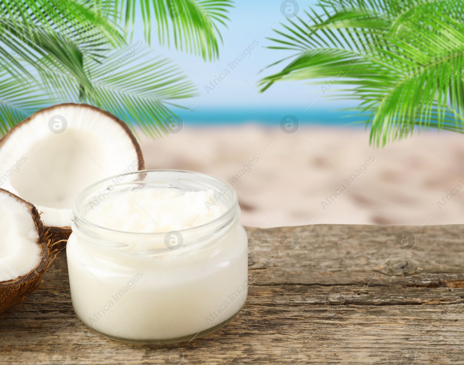 Cooking oil in jar and coconut on wooden table against beach. Space for text Image of Cooking oil in jar and coconut on wooden table against beach. Space for text