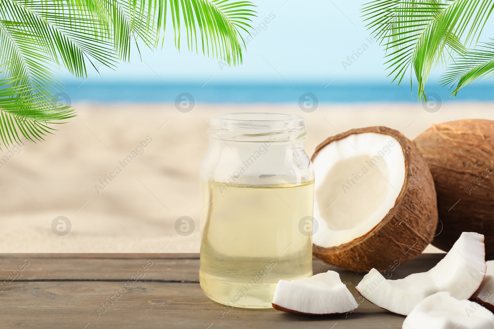 Cooking oil in jar and coconuts on wooden table against beach. Space for text Image of Cooking oil in jar and coconuts on wooden table against beach. Space for text