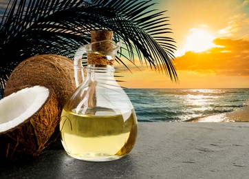 Image of Cooking oil in glass bottle and coconuts on table against beach. Space for text