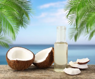 Image of Cooking oil in glass bottle and coconuts on wooden table against sea