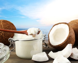 Image of Cooking oil in jar and coconuts on wooden table against sea