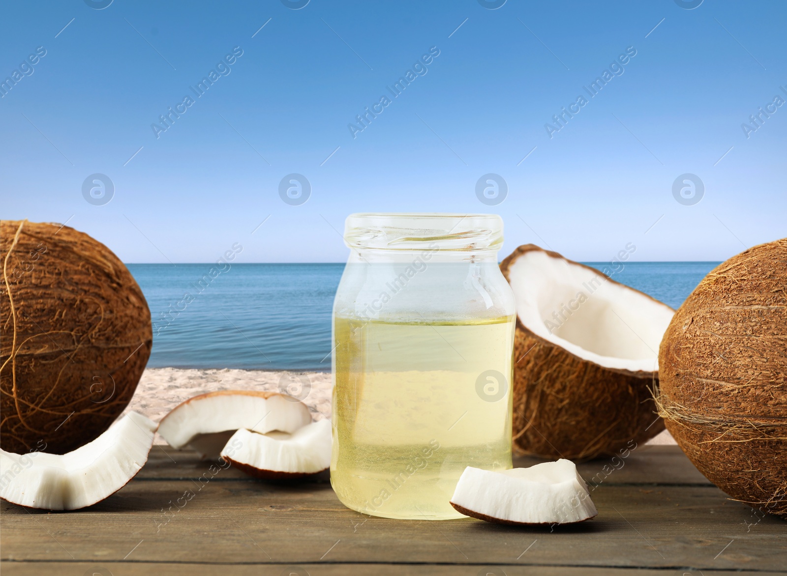 Cooking oil in jar and coconuts on wooden table against beach Image of Cooking oil in jar and coconuts on wooden table against beach