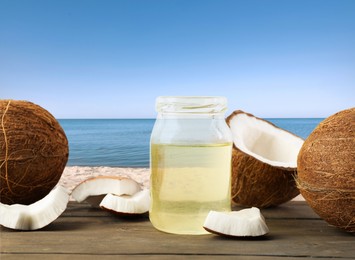 Image of Cooking oil in jar and coconuts on wooden table against beach