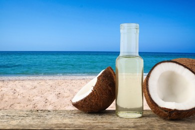 Image of Cooking oil in glass bottle and coconuts on wooden table against beach. Space for text