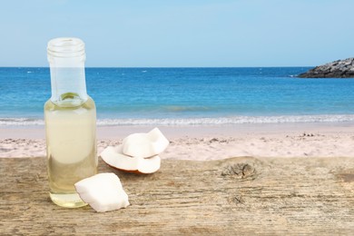 Image of Cooking oil in glass bottle and coconut pieces on wooden table against beach. Space for text