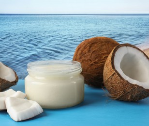 Image of Cooking oil in jar and coconuts on blue table against beach