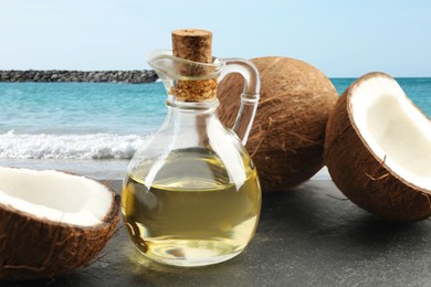 Image of Cooking oil in glass bottle and coconuts on table against beach