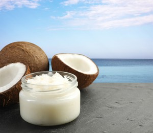 Image of Cooking oil in jar and coconuts on table against beach. Space for text