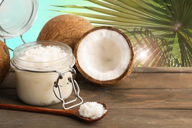 Image of Cooking oil in jar and coconuts on wooden table against palm leaves. Space for text