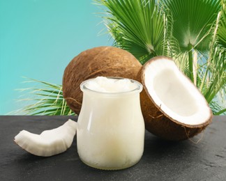 Image of Cooking oil in jar and coconuts on blue table against palm leaves