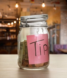 Image of Tips jar with money on light wooden table in cafe