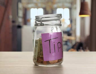 Image of Tips jar with money on light wooden table in cafe