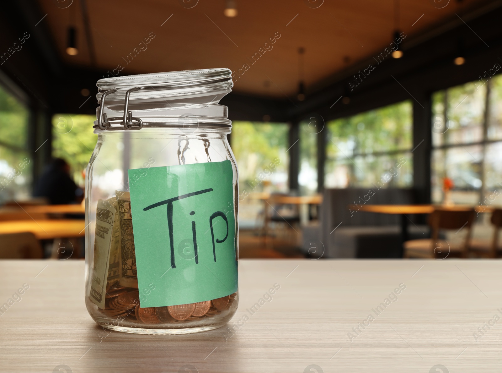 Tips jar with money on light wooden table in cafe, space for text Image of Tips jar with money on light wooden table in cafe, space for text