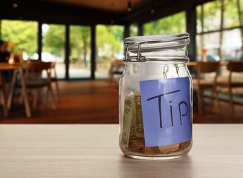 Image of Tips jar with money on light wooden table in cafe, space for text
