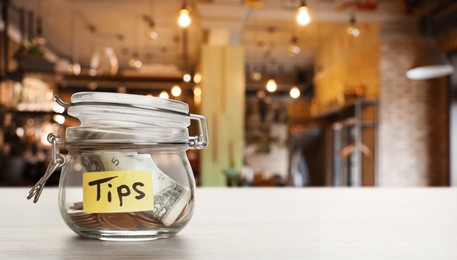 Image of Tips jar with money on white wooden table in cafe, space for text. Banner