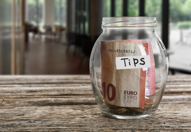 Image of Tips jar with money on wooden table in cafe, space for text