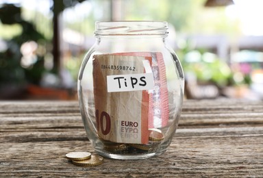 Image of Tips jar with money on wooden table in cafe