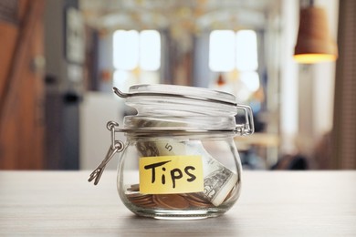 Image of Tips jar with money on light wooden table in cafe