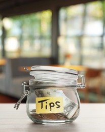 Image of Tips jar with money on light wooden table in cafe