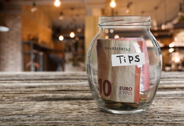Image of Tips jar with money on wooden table in cafe, space for text