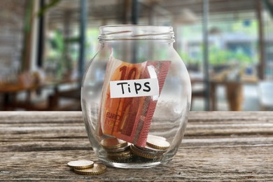 Image of Tips jar with money on wooden table in cafe