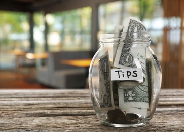 Image of Tips jar with money on wooden table in cafe, space for text