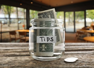 Image of Tips jar with money on wooden table in cafe