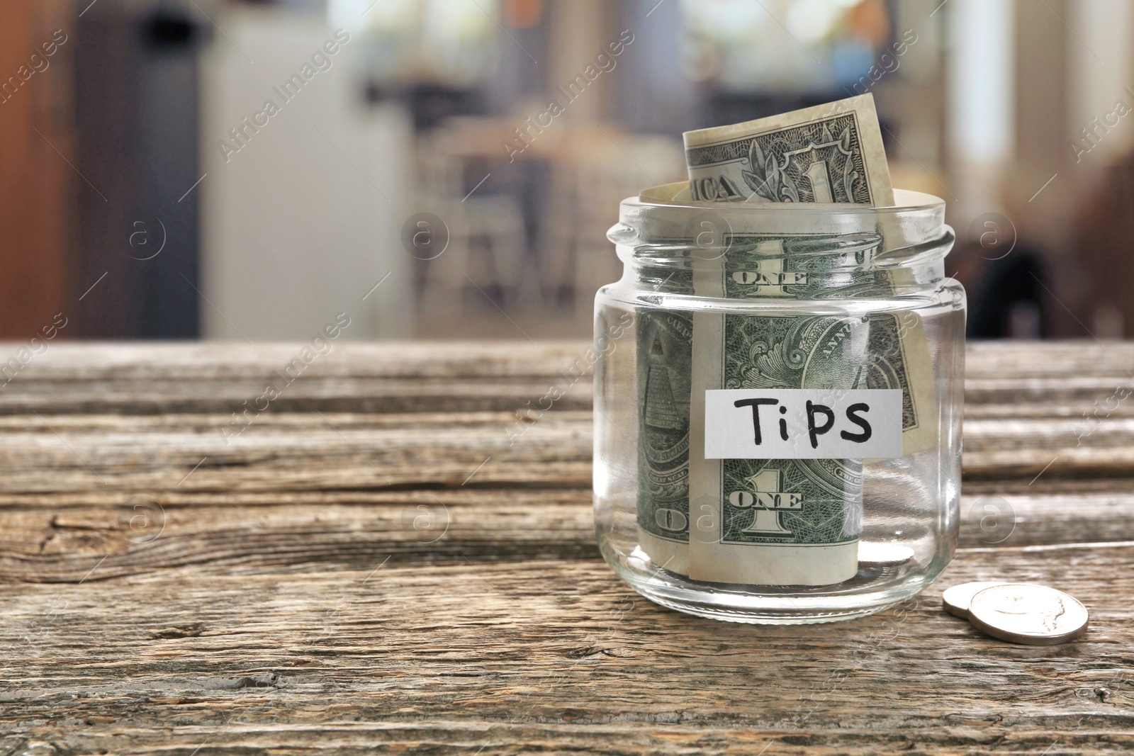 Tips jar with money on wooden table in cafe, space for text Image of Tips jar with money on wooden table in cafe, space for text