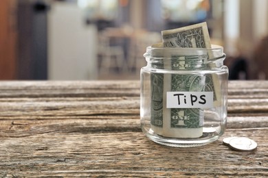 Image of Tips jar with money on wooden table in cafe, space for text