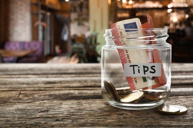 Image of Tips jar with money on wooden table in cafe, space for text