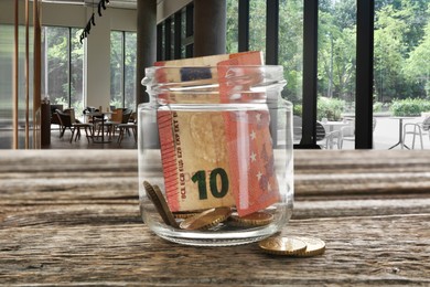 Image of Tips jar with money on wooden table in cafe