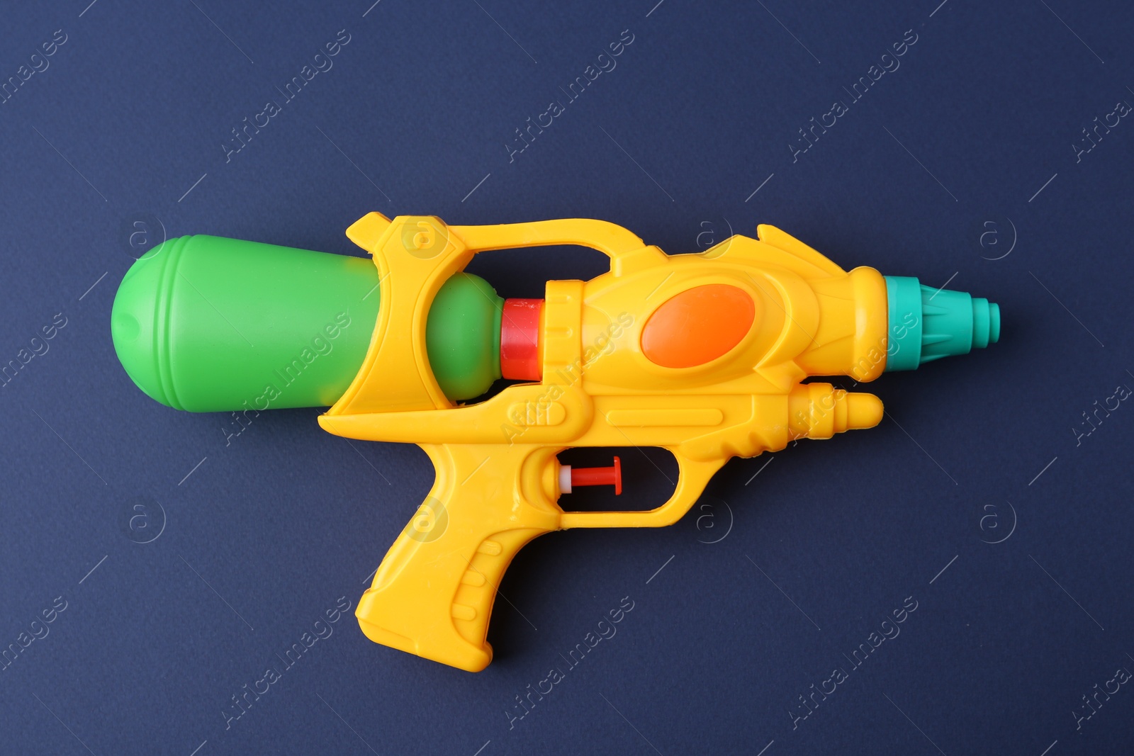 Bright plastic water gun on dark blue background, top view Photo of Bright plastic water gun on dark blue background, top view