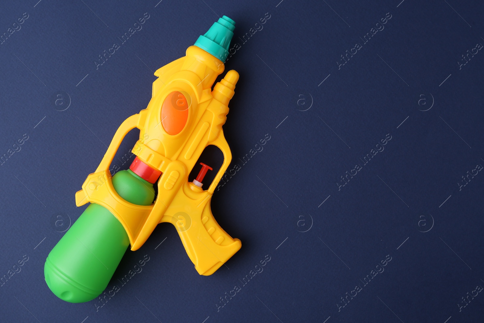 Bright plastic water gun on dark blue background, top view. Space for text Photo of Bright plastic water gun on dark blue background, top view. Space for text