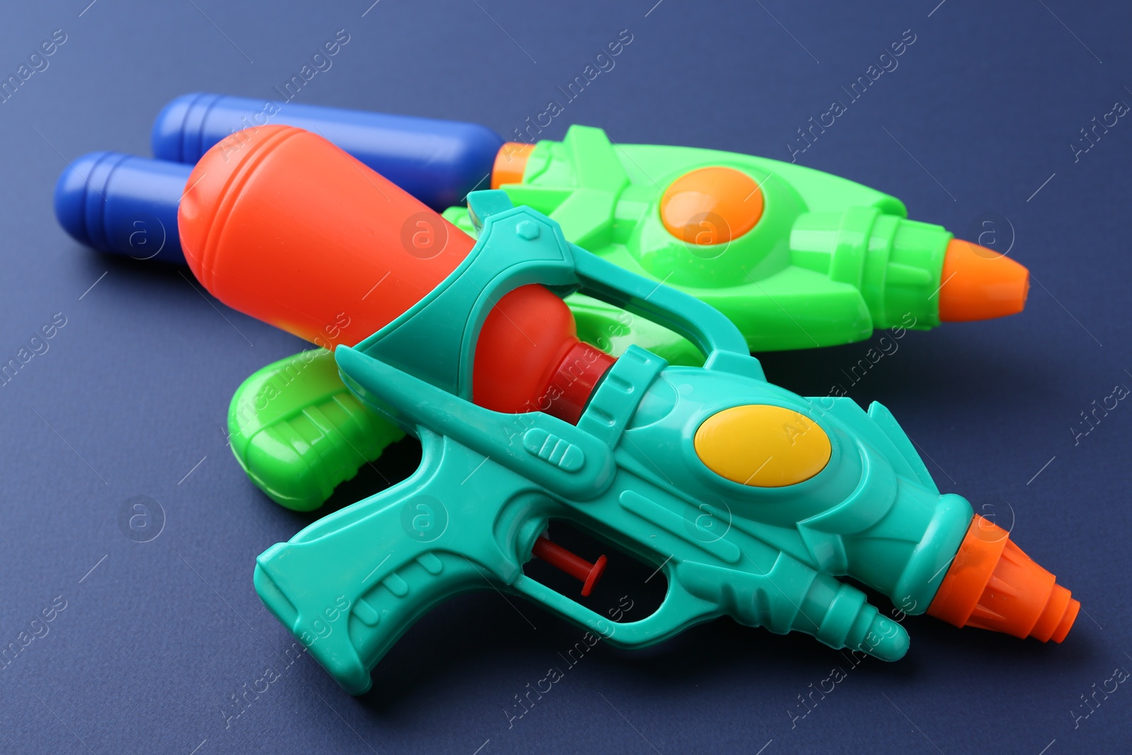 Bright plastic water guns on dark blue background, closeup Photo of Bright plastic water guns on dark blue background, closeup