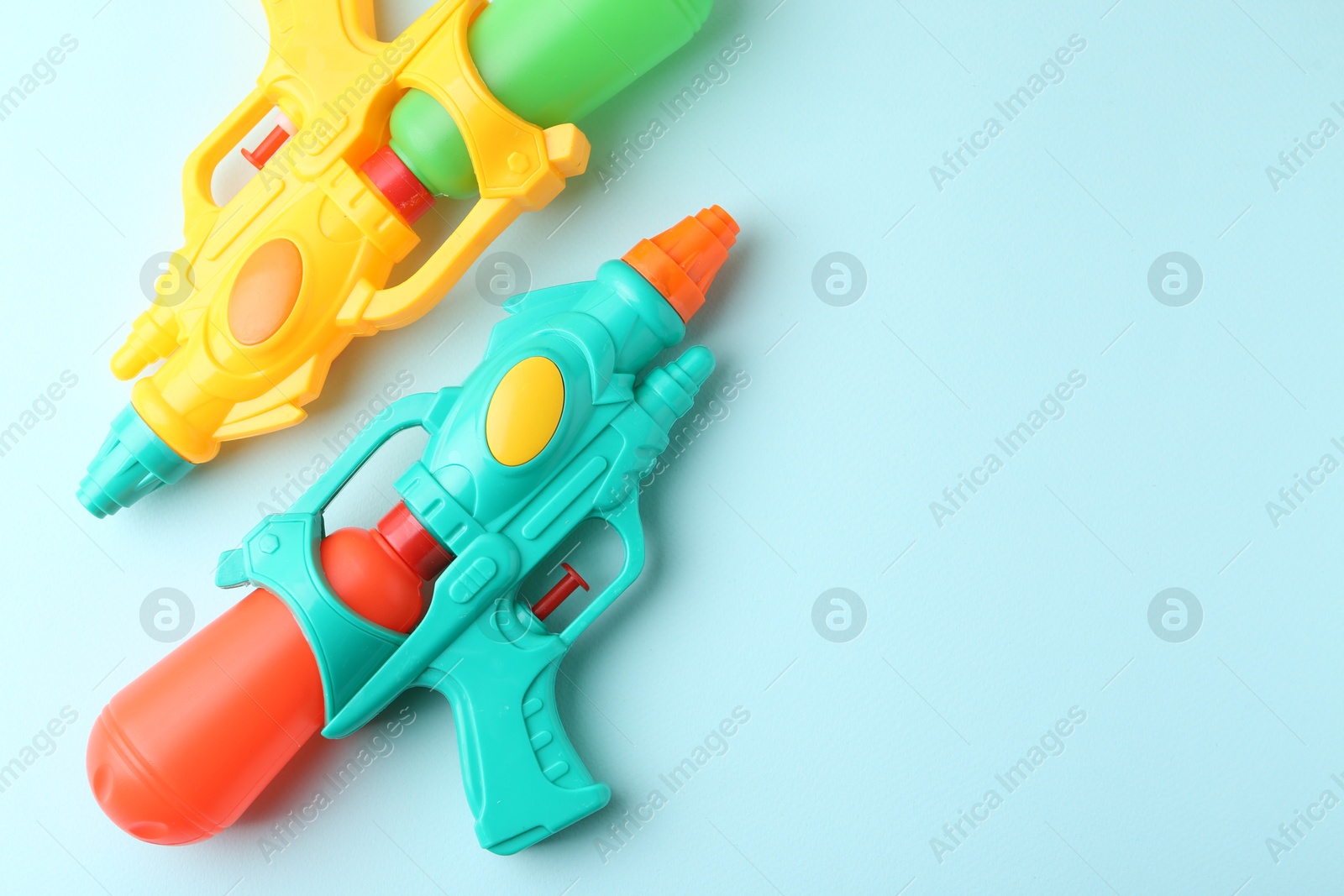 Photo of Bright plastic water guns on light blue background, top view. Space for text