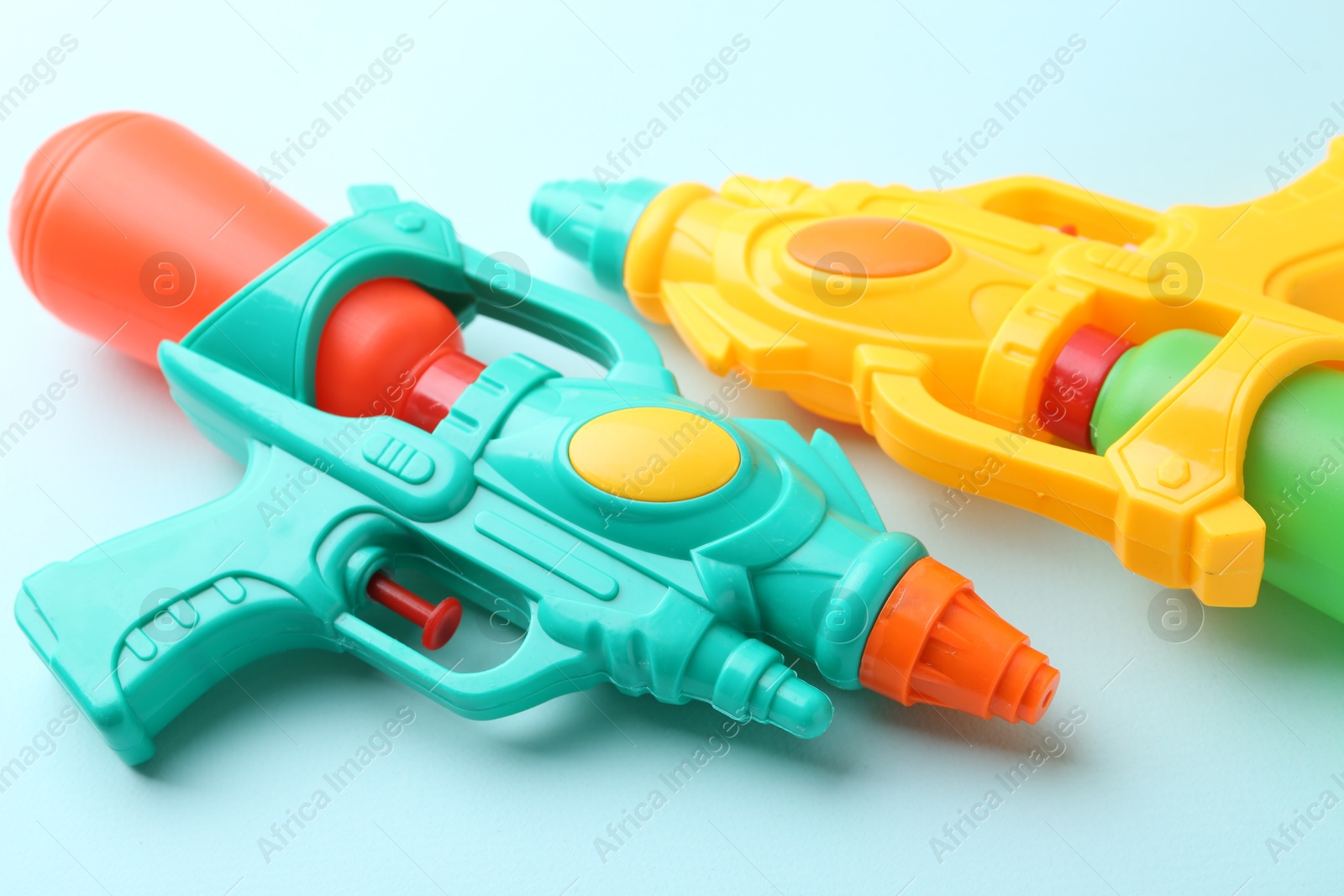 Bright plastic water guns on light blue background, closeup Photo of Bright plastic water guns on light blue background, closeup