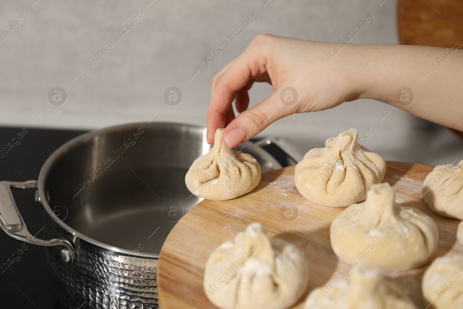 Photo of Woman putting khinkali into pot indoors, closeup