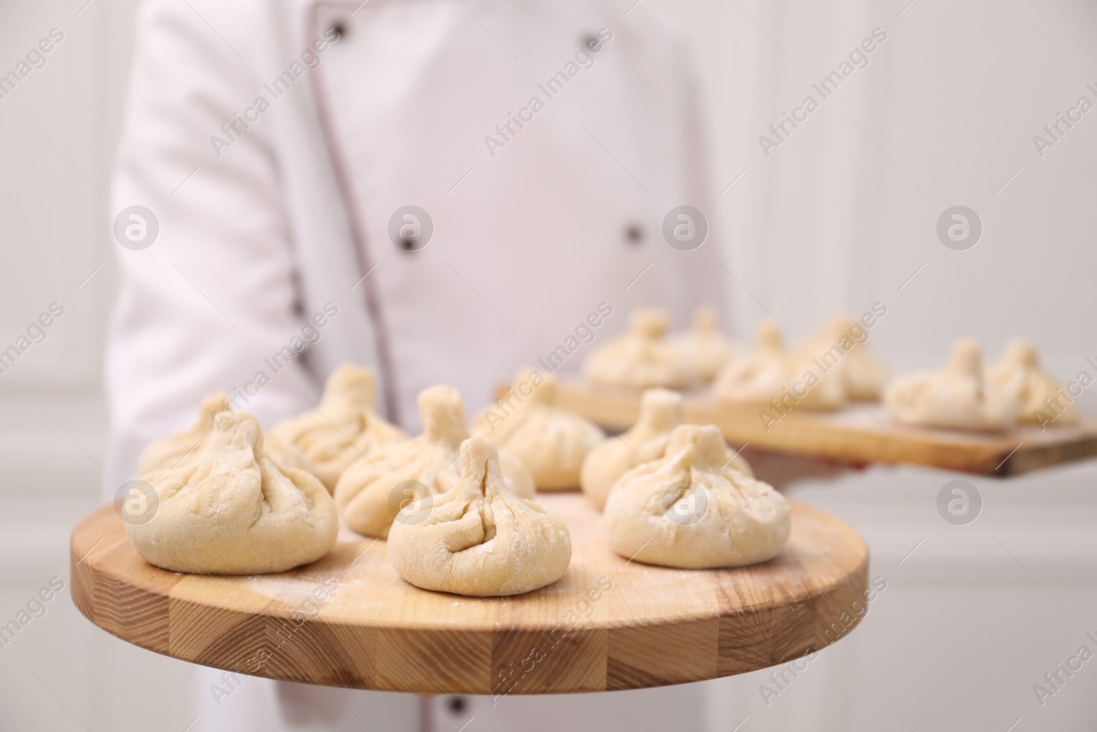 Chef holding board with uncooked khinkali indoors, closeup Photo of Chef holding board with uncooked khinkali indoors, closeup