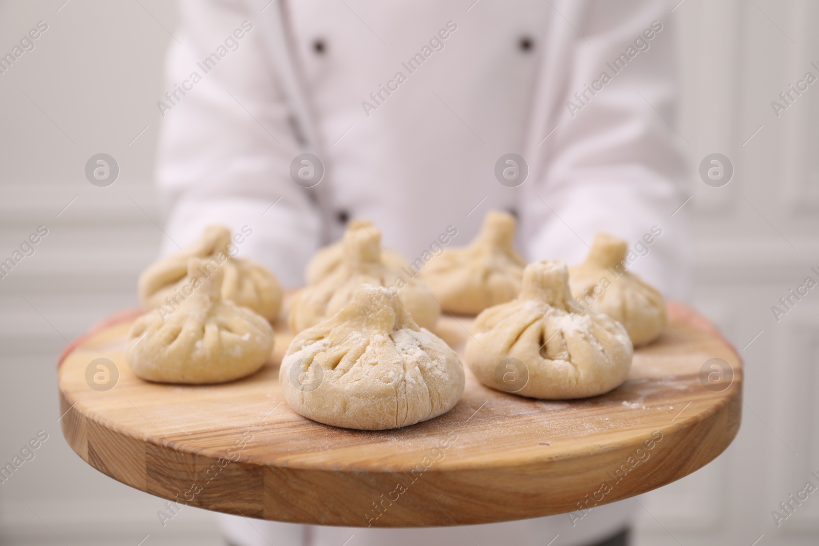 Chef holding board with uncooked khinkali indoors, closeup Photo of Chef holding board with uncooked khinkali indoors, closeup