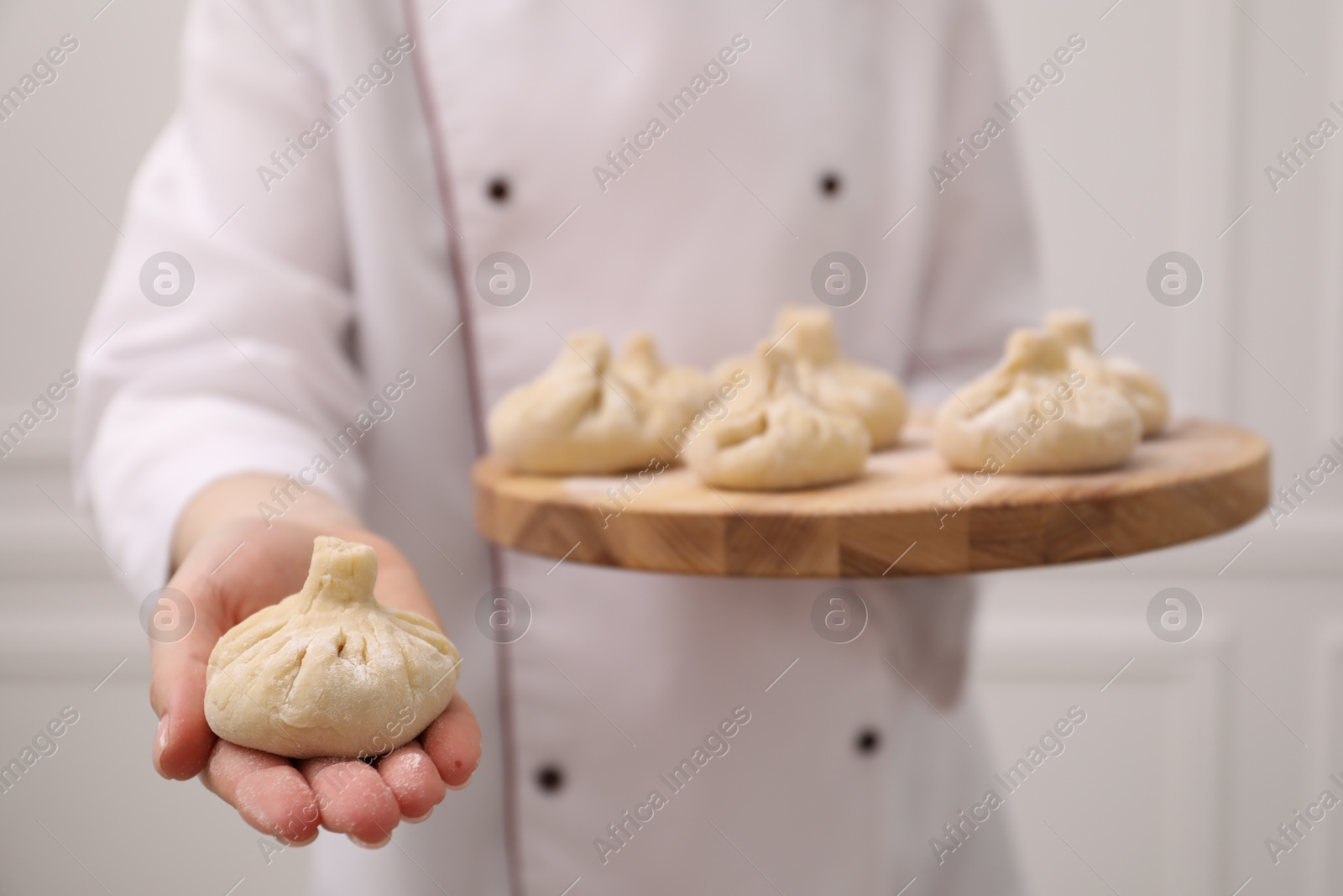 Chef holding board with uncooked khinkali indoors, closeup Photo of Chef holding board with uncooked khinkali indoors, closeup