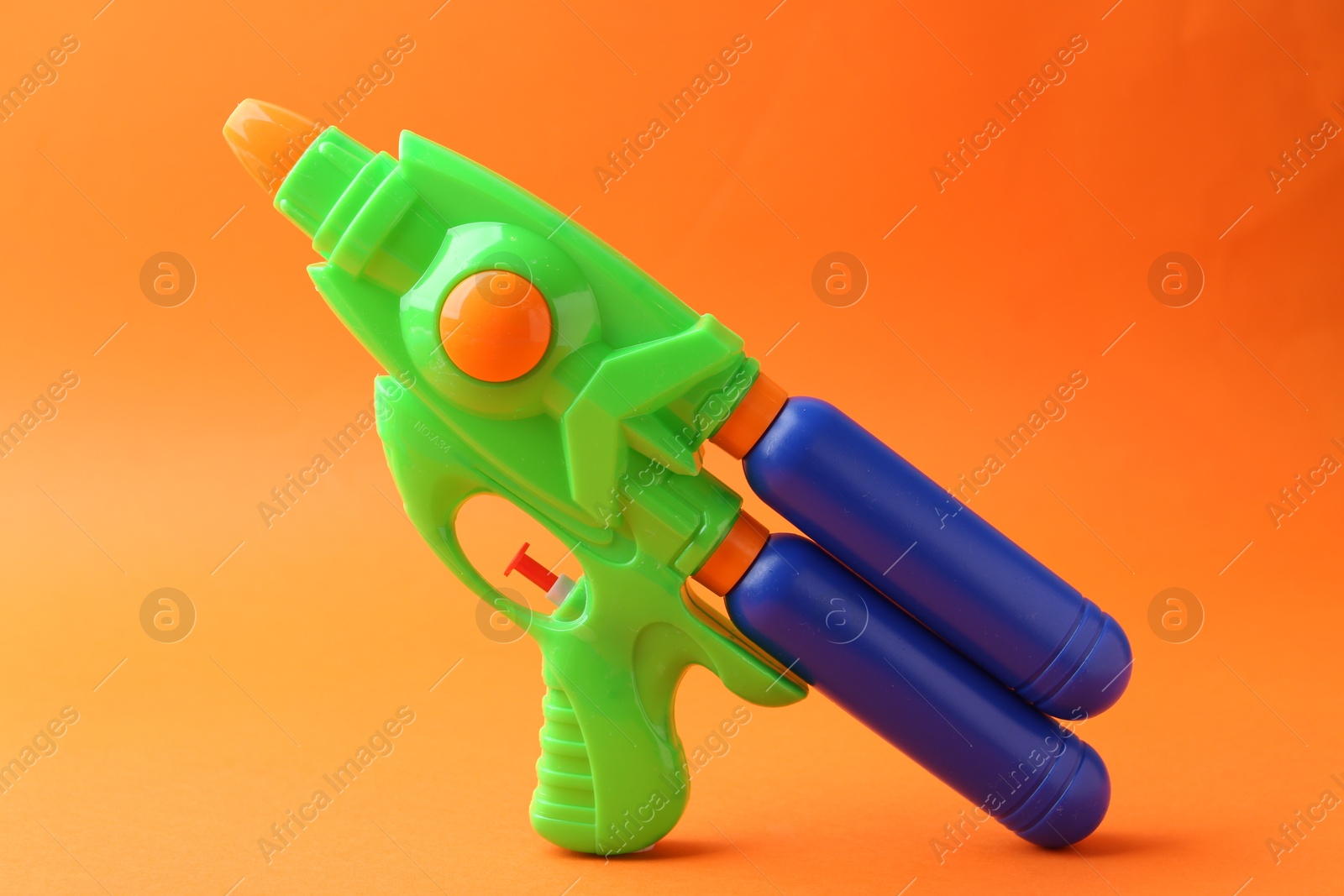 Bright plastic water gun on orange background Photo of Bright plastic water gun on orange background