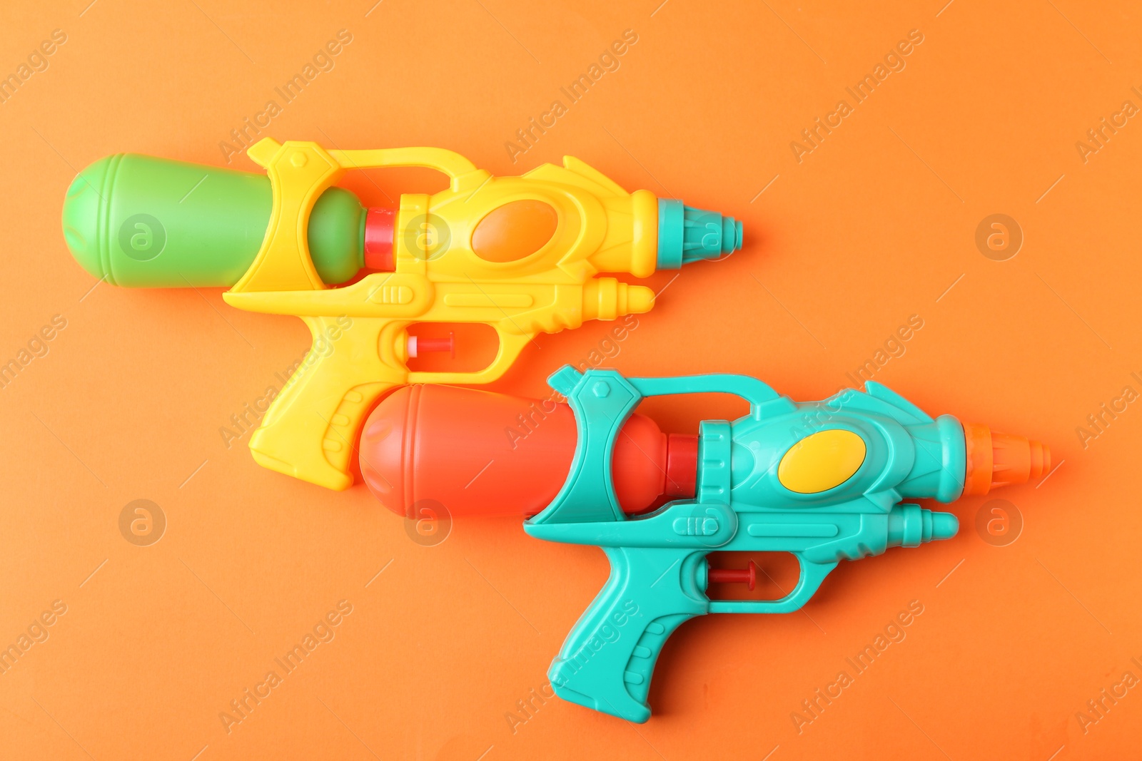 Bright plastic water guns on orange background, top view Photo of Bright plastic water guns on orange background, top view