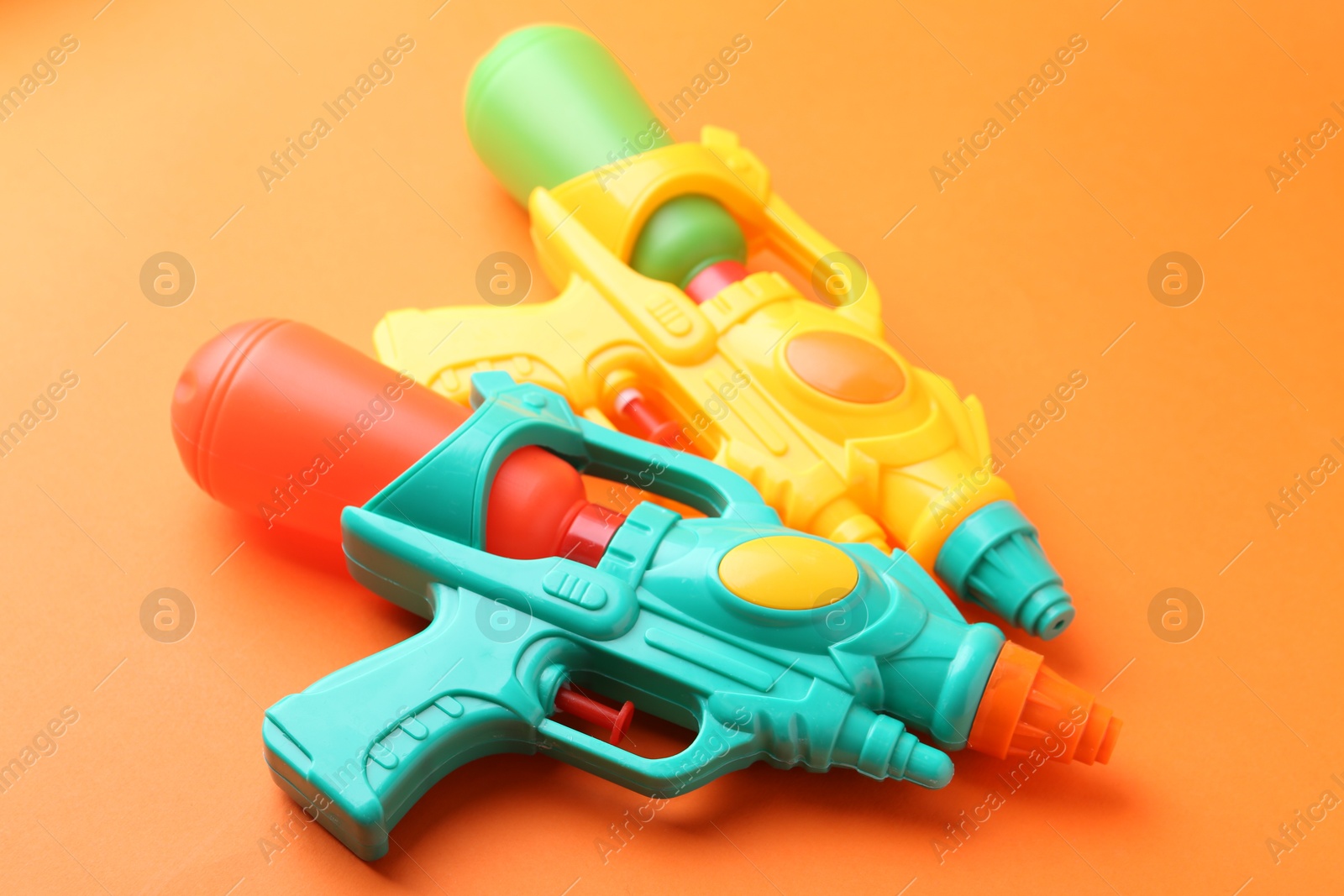 Bright plastic water guns on orange background, closeup Photo of Bright plastic water guns on orange background, closeup