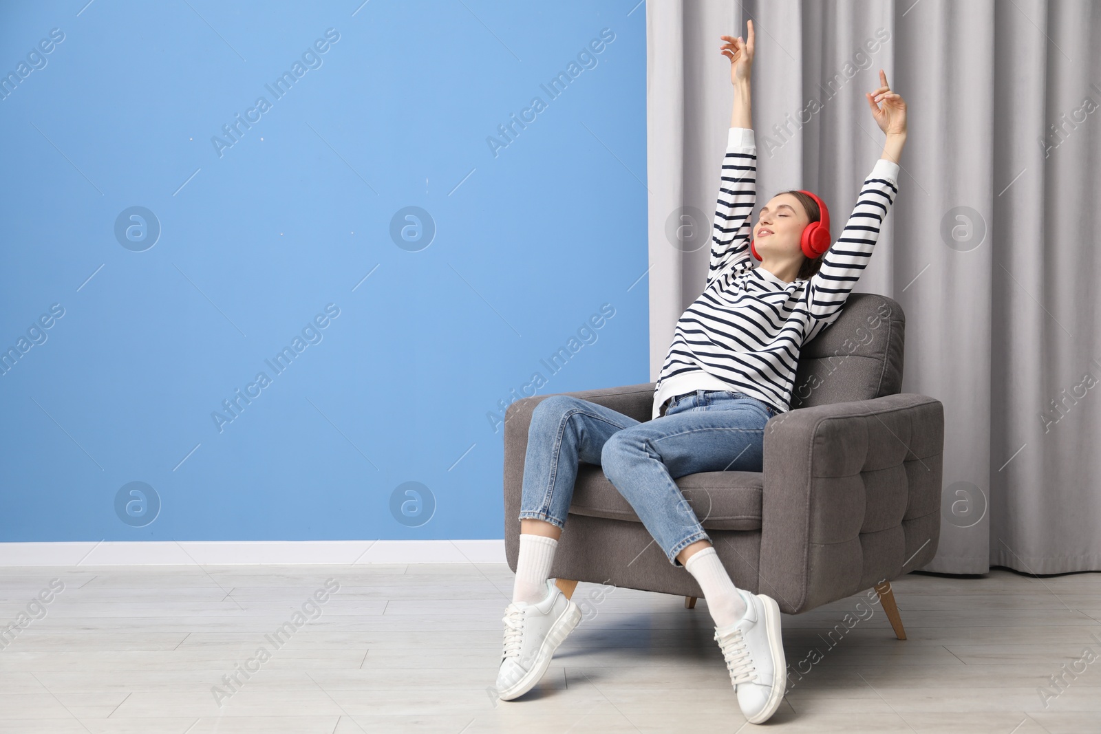 Beautiful woman with headphones relaxing in comfortable armchair near blue wall indoors, space for text Photo of Beautiful woman with headphones relaxing in comfortable armchair near blue wall indoors, space for text