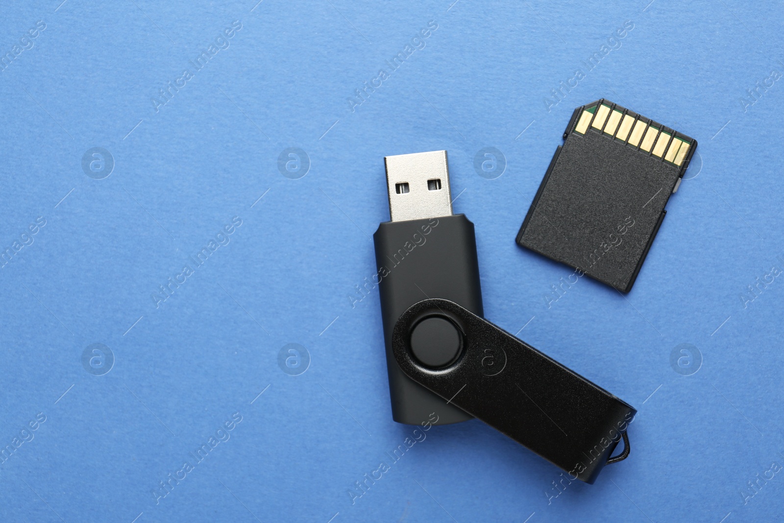 Flash drive and SD memory card on blue background, flat lay. Space for text Photo of Flash drive and SD memory card on blue background, flat lay. Space for text